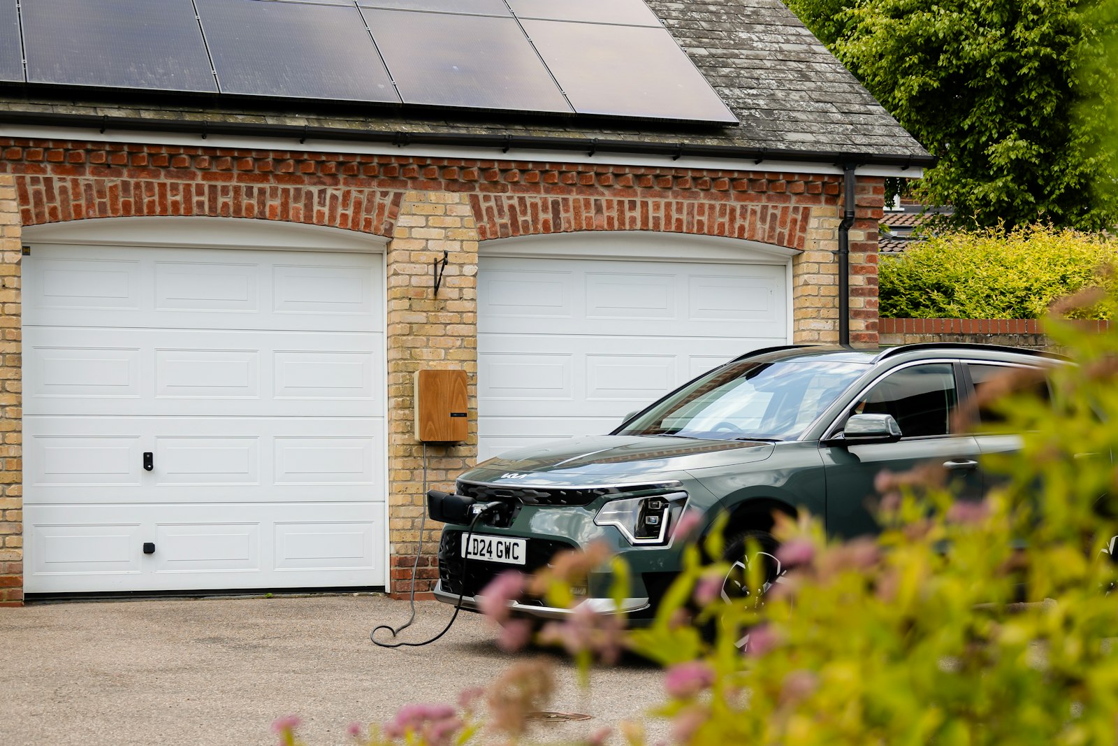 Elbil lades hjemme foran garasje med solcellepanel på taket