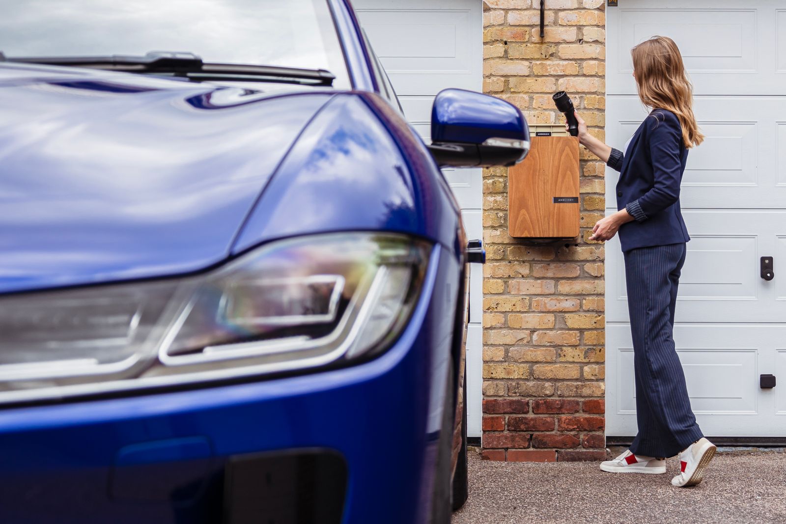 Kvinne lader elbilen ved en hjemmeladestasjon